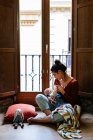 Happy mother breastfeeding baby near window — Stock Photo