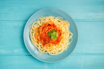 Top view of blue ceramic plate with pasta and tomato sauce decorated with parsley on light blue wooden background — Stock Photo
