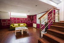 Soggiorno contemporaneo con pavimento in legno e con divano verde brillante ed elementi geometrici su pareti rosse — Foto stock