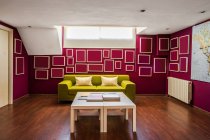 Sala de estar contemporânea com piso de madeira e com sofá verde brilhante e elementos geométricos em paredes vermelhas — Fotografia de Stock
