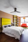 Комфортабельная кровать с ярко-желтым изголовьем в современной однокомнатной квартире, оформленной в стиле минимализма — стоковое фото