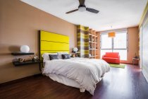 Cama confortável com cabeceira amarela brilhante no moderno apartamento estúdio decorado em estilo minimalista — Fotografia de Stock
