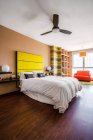 Комфортабельная кровать с ярко-желтым изголовьем в современной однокомнатной квартире, оформленной в стиле минимализма — стоковое фото