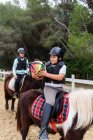 Adolescents garçons dans des casques jetant ballon les uns aux autres tout en chevauchant des chevaux sur l'arène de dressage au cours de l'école équestre — Photo de stock