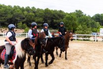 Adolescentes jockeys em capacetes se comunicando uns com os outros enquanto montam cavalos obedientes na arena de curativo arenoso durante a aula na escola equestre — Fotografia de Stock