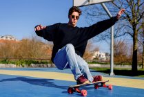Young handsome male with raised arms falling from skateboard while trying to do trick on sunny day on sports ground — Stock Photo