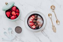 From above slices of ripe strawberries and blackberries in cinnamon powder in yogurt bowl in composition with bowl with fresh whole berries and golden teaspoons on white table — Stock Photo