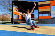 Молодий красивий чоловік з піднятими руками падає зі скейтборду, намагаючись зробити трюк у сонячний день на спортивному майданчику — стокове фото