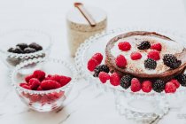 High angle of tasty sweet tart with creamy filling and fresh blackberry and raspberry on glass stand in composition with bowls of fresh berries — Stock Photo