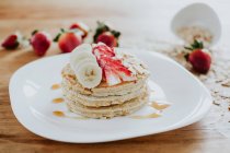 Closeup stack of yummy pancakes with pieces of banana and strawberry served on plate with almond flakes and honey during breakfast — Stock Photo