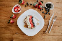 Stapel leckerer Pfannkuchen auf Teller serviert mit Bananenstücken und Erdbeeren und frischen Blaubeeren mit Kokosflocken zum Frühstück — Stockfoto