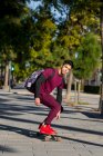 Ganzkörper junger hispanischer Mann mit Rucksack fährt Skateboard auf dem Bürgersteig an einem sonnigen Tag auf der Stadtstraße — Stockfoto