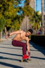 Все тело молодого латиноамериканца с рюкзаком на скейтборде на тротуаре в солнечный день на городской улице — стоковое фото