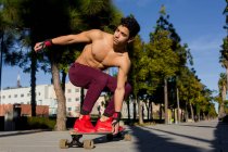 Corpo pieno giovane uomo ispanico con zaino equitazione skateboard sul marciapiede nella giornata di sole sulla strada della città — Foto stock