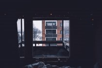 Apartment building located on snowy street behind balcony and window of cozy dark room — Stock Photo
