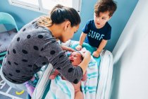 Von oben von vorsichtiger Frau und kleinem Sohn in Freizeitkleidung windelndes niedliches weinendes Baby nach dem Bad im Blaulicht-Kinderzimmer — Stockfoto