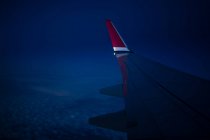 A través de la ventana vista del ala del avión moderno volando sobre las nubes en la noche oscura - foto de stock