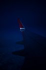 Крізь вікно вигляд крила сучасного літака, що літає над хмарами в темну ніч — стокове фото
