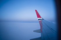 Через окно вид крыла современного самолета, летящего над облаками в темное ночное время — стоковое фото