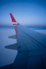Через окно вид крыла современного самолета, летящего над облаками в темное ночное время — стоковое фото