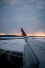 Wing of modern airplane on snowy terrain against dark forest at horizon and aircraft taking off from runway to gray sky in overcast weather at dusk in Norway — Stock Photo