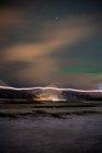 Живописные пейзажи с освещенными поселениями на берегу пролива у подножия снежных гор под облачным звездным небом с удивительными зелеными северными сияниями в Лофотене — стоковое фото