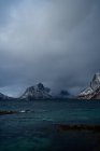 Дивовижний вигляд блакитної рифленої морської води проти сніжних гірських кряжів на березі під сірим хмарним небом взимку в Норвегії. — стокове фото