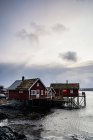 Маленькие красные загородные дома с деревянными пирсами на скальном пляже пролива со спокойной водой прохладным вечером в Норвегии — стоковое фото