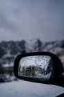 Wet side rear view mirror of modern black auto with melting snow against blurred snowy highland under gray cloudy sky in winter Norway — Stock Photo