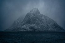 Захватывающий дух вид голубой волнистой морской воды на снежные горные хребты на берегу под серым облачным небом зимой в Норвегии — стоковое фото