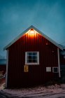 Cottage a strisce rosso scuro con finestre bianche e tetto innevato nella piccola città con tempo coperto a Lofoten — Foto stock