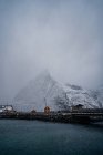 Snowy orange country houses on coast of strait with rippled water in cold overcast weather in Lofoten — Stock Photo