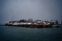 Maisons de campagne orangées enneigées sur la côte du détroit avec eau ondulée par temps froid et couvert à Lofoten — Photo de stock