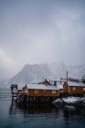 Maisons de campagne jaunes sur la côte du détroit contre les crêtes de montagne enneigées brumeuses par temps couvert en Norvège — Photo de stock