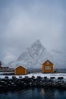 Maisons de campagne orangées enneigées sur la côte du détroit avec eau ondulée par temps froid et couvert à Lofoten — Photo de stock
