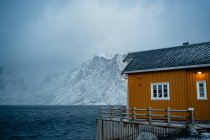 Жовті сільські будинки на узбережжі протоки проти туманних снігових гірських гребенів у спеку в Норвегії. — стокове фото