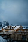 Case di campagna gialle sulla costa dello stretto contro creste nevose nebbiose in tempo nuvoloso in Norvegia — Foto stock