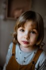 From above adorable little girl in casual outfit looking at camera while standing on blurred background of cozy room at home — Stock Photo