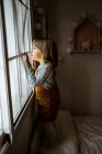 Чарівна маленька дівчинка в повсякденному одязі дивиться у вікно, відпочиваючи в затишній кімнаті вдома — стокове фото