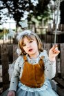 Чарівна маленька дівчинка в казковому костюмі, сидячи на похмурій дерев'яній лавці і дивлячись на камеру, проводячи час у дворі — стокове фото