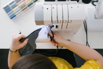 Dall'alto ritagliato donna adulta bruna irriconoscibile utilizzando la macchina da cucire per fare indumento in denim mentre si lavora in officina a casa — Foto stock