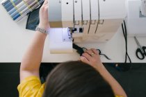 From above cropped unrecognizable brunette adult woman using sewing machine to make denim garment while working in home workshop — Stock Photo