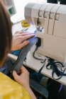 De cima cortada mulher adulta morena irreconhecível usando máquina de costura para fazer roupas de ganga enquanto trabalhava em oficina em casa — Fotografia de Stock