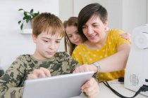 Adult woman and children browsing modern tablet together while sitting at table at home — Stock Photo