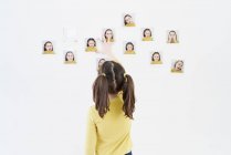 Menina bonito em um vestido amarelo está de pé em suas costas colocando fotos de si mesma mostrando várias emoções — Fotografia de Stock