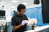 Афроамериканец в латексных перчатках с зеркалом во рту и зондом для проверки ложных зубов во время работы в современной лаборатории — стоковое фото