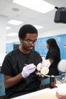Afro-Américain dans des gants en latex en utilisant un miroir de bouche et une sonde pour vérifier les fausses dents tout en travaillant dans un laboratoire moderne — Photo de stock