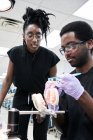 Niedriger Winkel einer glücklichen Afroamerikanerin mit Dreadlocks und einem bärtigen Mann, der während der Arbeit im Labor lächelt und sich falsche Zähne putzt — Stockfoto