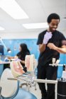 False teeth attached to metal occludator on blurred background of modern orthodontic lab and ethnic staff — Stock Photo