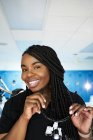 Щаслива чорна жінка з косами посміхається і дивиться на камеру, перш ніж надягати бінокль під час роботи в сучасній лабораторії — стокове фото